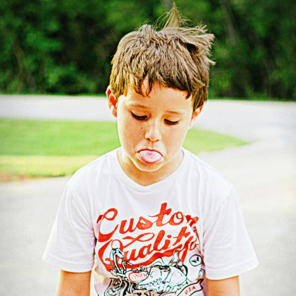 Bild eines Jungen, der zu Boden schaut und die Zunge herausstreckt – resignierte oder missmutige Stimmung
