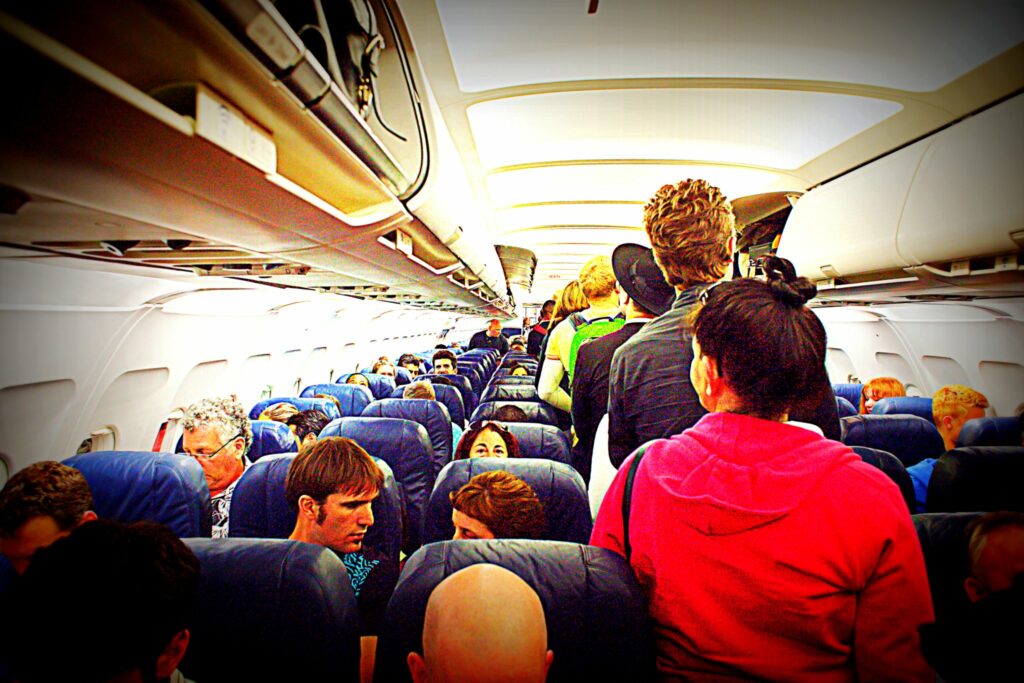 Flugzeuginnenraum mit Passagieren und einer Reihe stehender Passagiere im Mittelgang