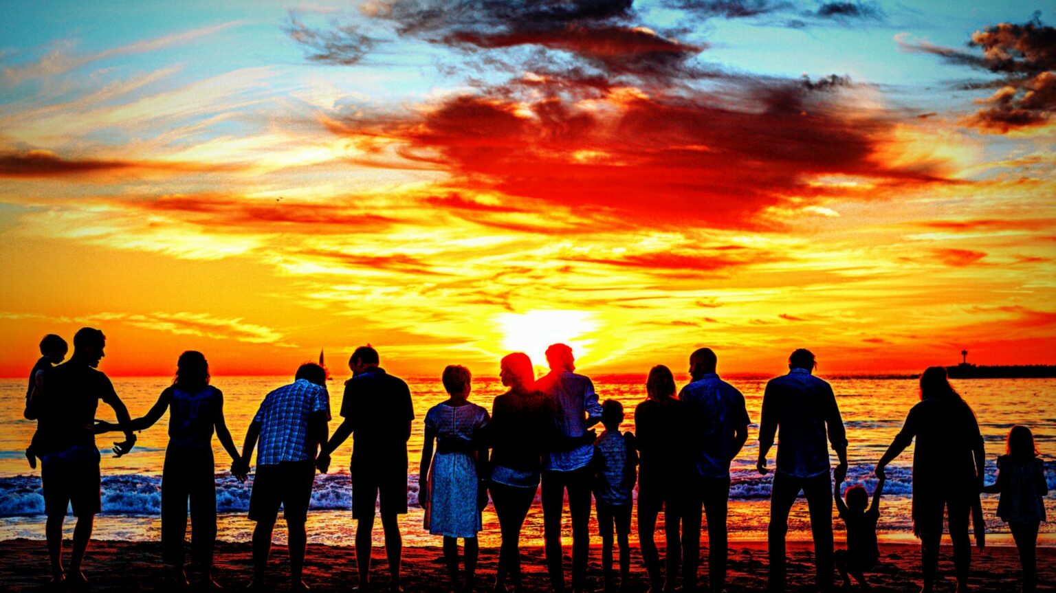 Bild mit verschiedenen Menschen im Gegenlicht als Silhouette vor einem Gewässer und dem Sonnenuntergang.